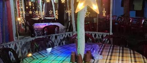 A restaurant with a checkered tablecloth, star-shaped lights, and a thatched roof.