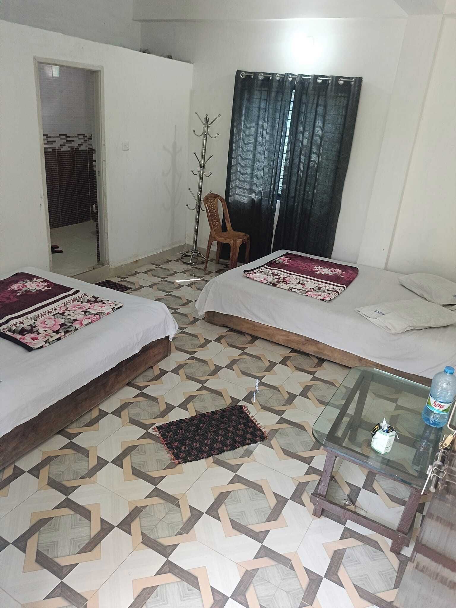 A room with two beds, a glass table, a chair, and a door leading to another room.