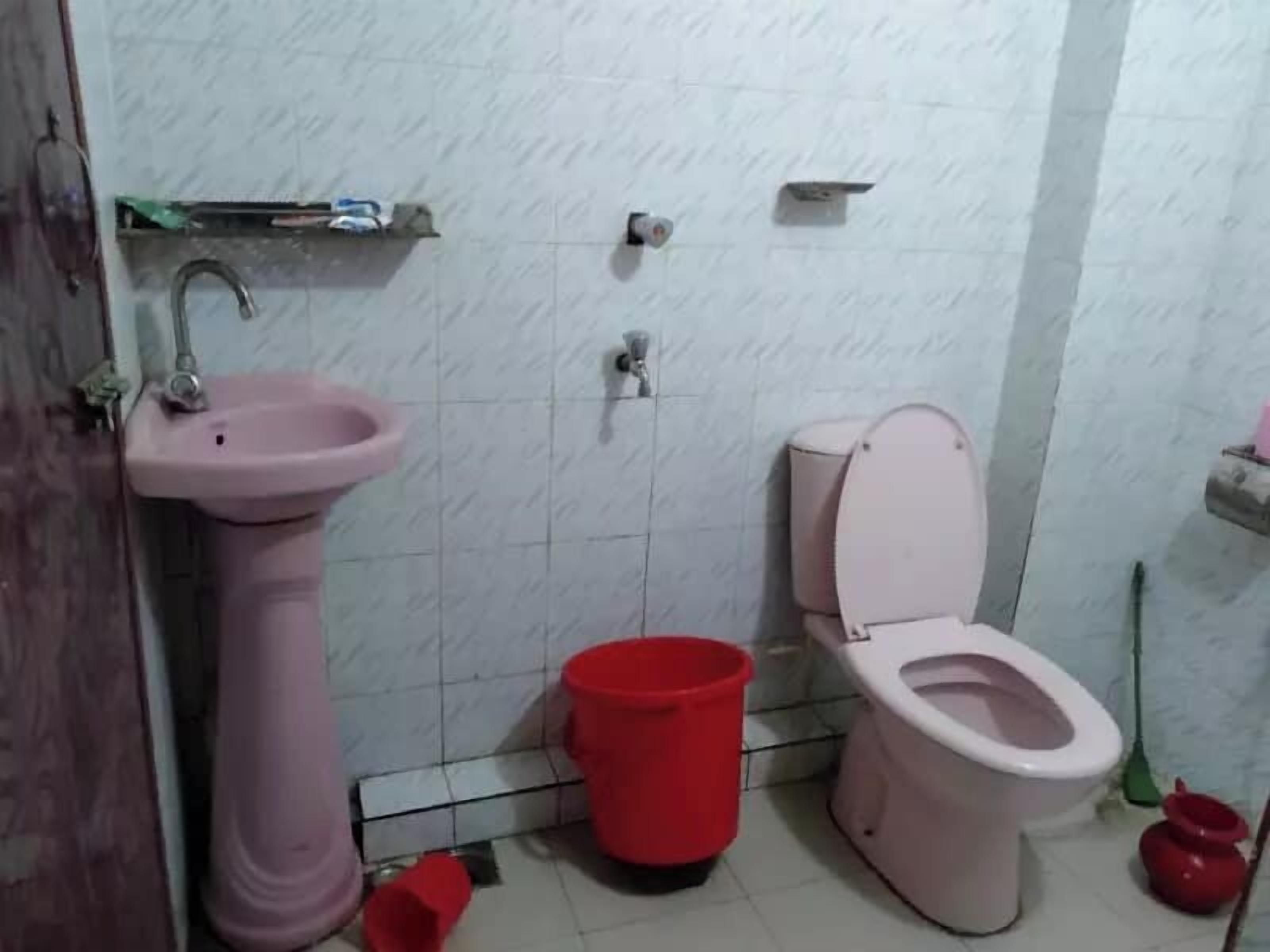 A bathroom with a pink sink, toilet, and red bucket.