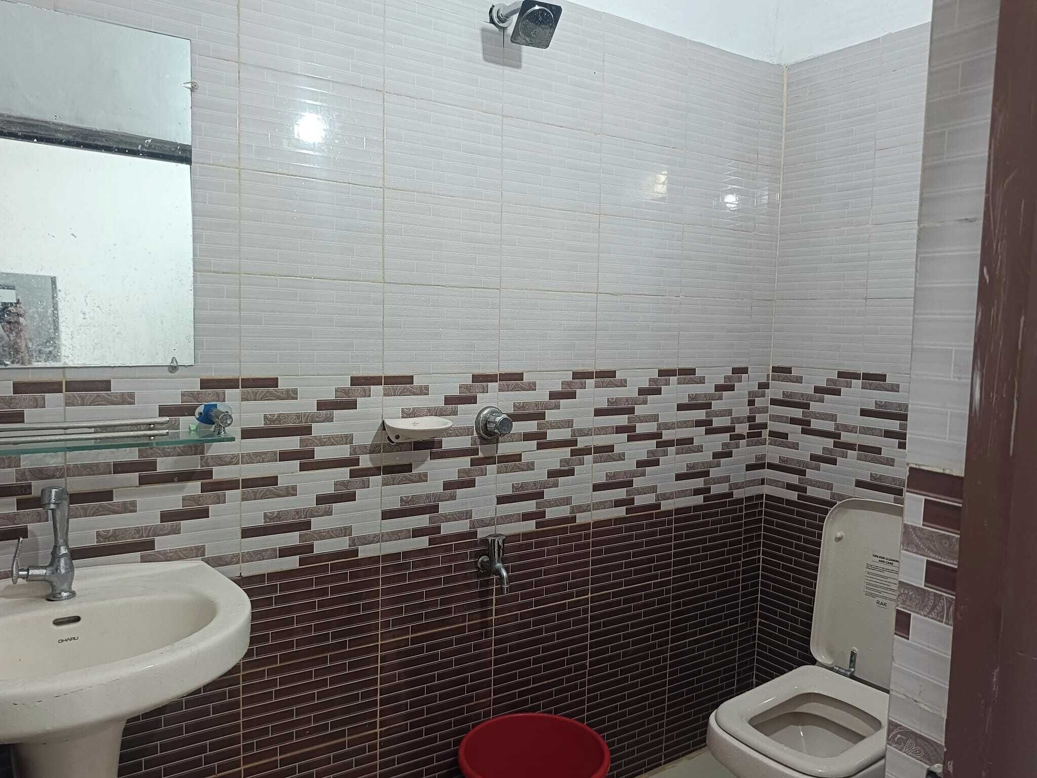 A bathroom with a white sink, a glass shelf, a red bucket, and a toilet.