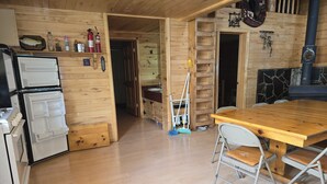 A wooden interior with a kitchen area featuring a refrigerator, a stove, and a wooden table with chairs. - Camp Jackson Family Cabin (San Juan County)
