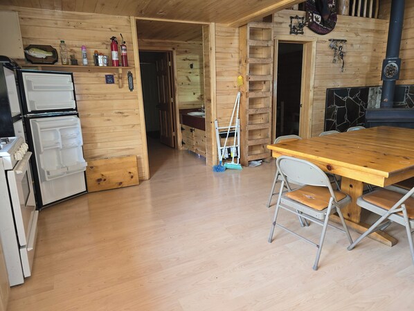 Un interior de madera con una zona de cocina que incluye un refrigerador, una estufa y una mesa de madera con sillas.
