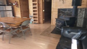 A wooden interior with a dining table and chairs, a fireplace, and a ladder leading to a door. - Camp Jackson Family Cabin (San Juan County)