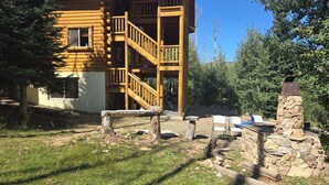 A wooden cabin with a staircase leading to a balcony, surrounded by a grassy yard and trees.