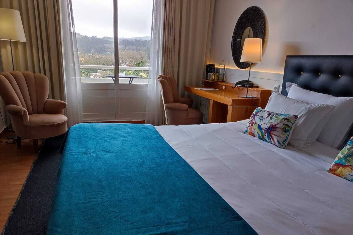 A hotel room with a bed, a desk, a chair, and a view of the outdoors.