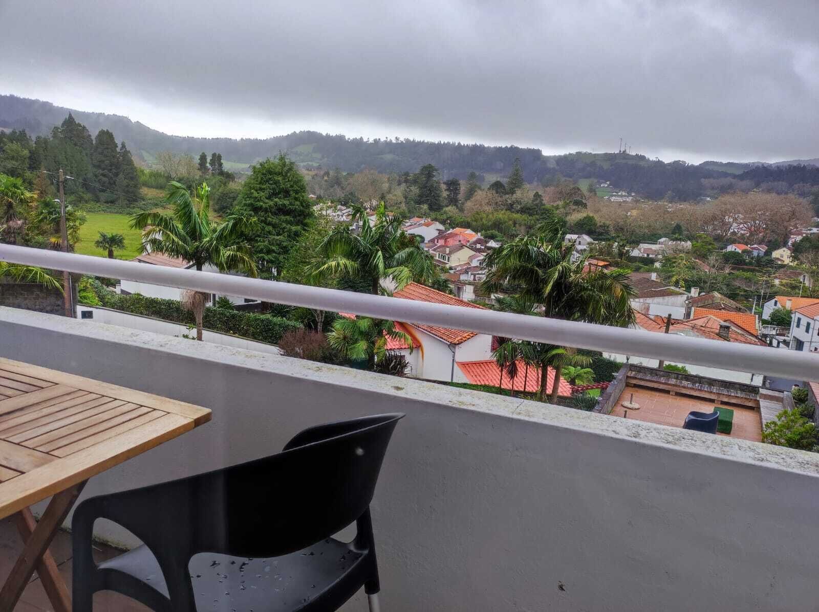 Un balcon donnant sur un quartier résidentiel, avec des maisons aux toits rouges et des palmiers.