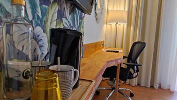 Une chambre d’hôtel avec un bureau en bois, une chaise de bureau noire, un téléviseur fixé au mur, une lampe et un papier peint à motifs floraux.