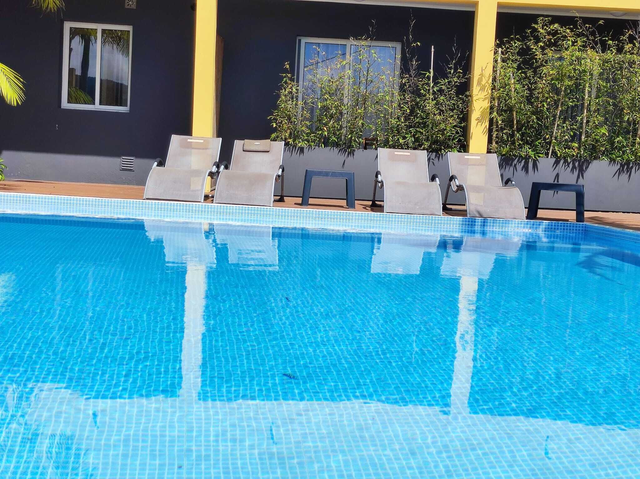 En klarblå pool med kakelbeklädda kanter, omgiven av solstolar och krukväxter.