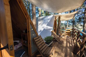 Una terraza de madera con toldo, sillas de madera y una mesita.