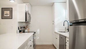 Een moderne keuken met witte kastjes, roestvrijstalen apparatuur en een houten vloer.