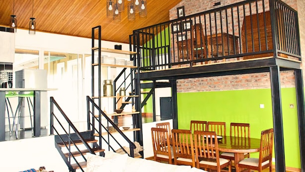 A dining area with a high table and chairs, a staircase with a railing, and a loft space with a railing and a view of the interior.