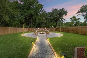 Un patio trasero con un área circular de grava, un brasero y una valla de madera.