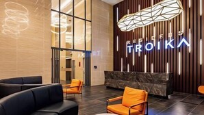Eine moderne Lobby mit einer Rezeption, schwarzen und orangefarbenen Sitzgelegenheiten sowie einer geometrischen Leuchte.