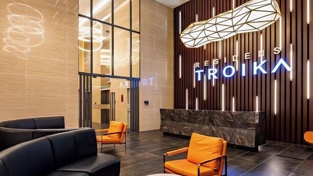 A modern lobby with a reception desk, black and orange seating, and a geometric light fixture.