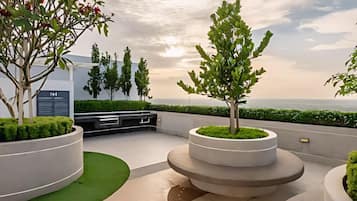 A rooftop garden with circular planters, a seating area, and a view of the sea.