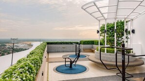 A rooftop terrace with outdoor exercise equipment, a covered seating area, and a view of the cityscape.