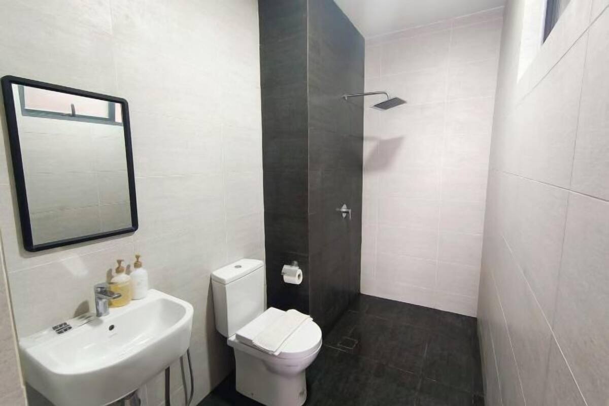 Un baño con lavamanos blanco, inodoro y ducha con azulejos oscuros.