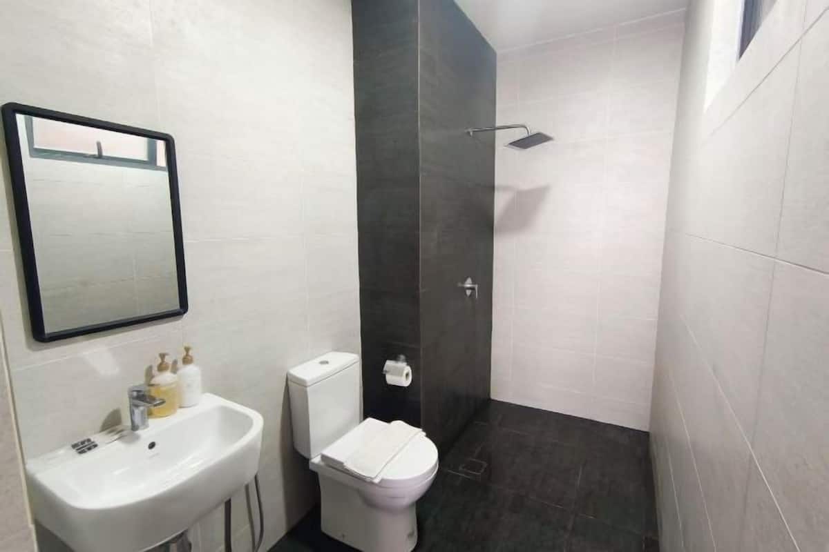 Une salle de bain avec un lavabo blanc, des toilettes et une douche carrelée de couleur foncée.