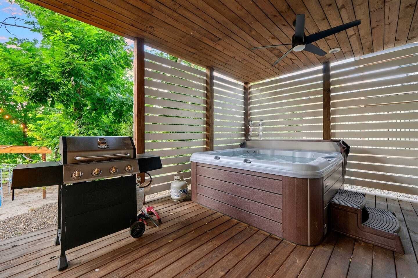 A covered outdoor area with a barbecue grill, a hot tub, and a ceiling fan.