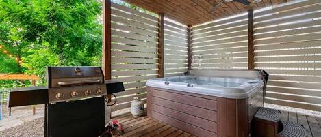 A covered outdoor area with a barbecue grill, a hot tub, and a ceiling fan.