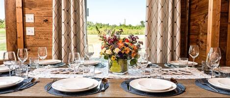 A dining table set for a meal with a floral centerpiece, surrounded by wooden walls and curtains.