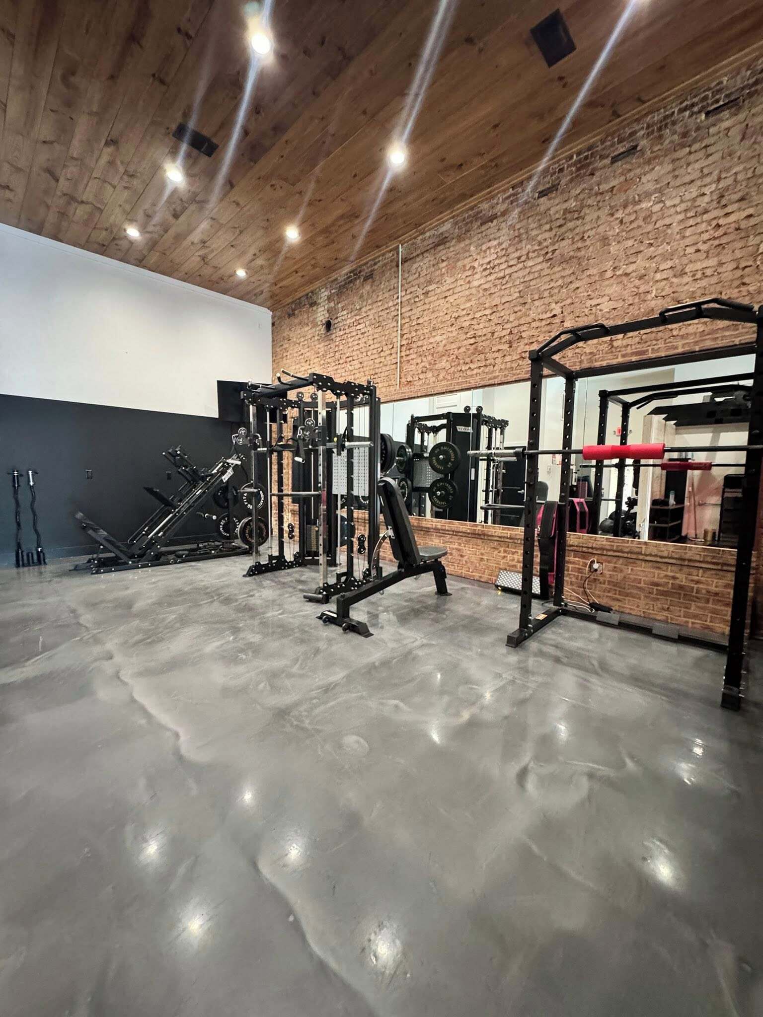 Un gimnasio con equipo de levantamiento de pesas, suelo de hormigón y pared de ladrillo.