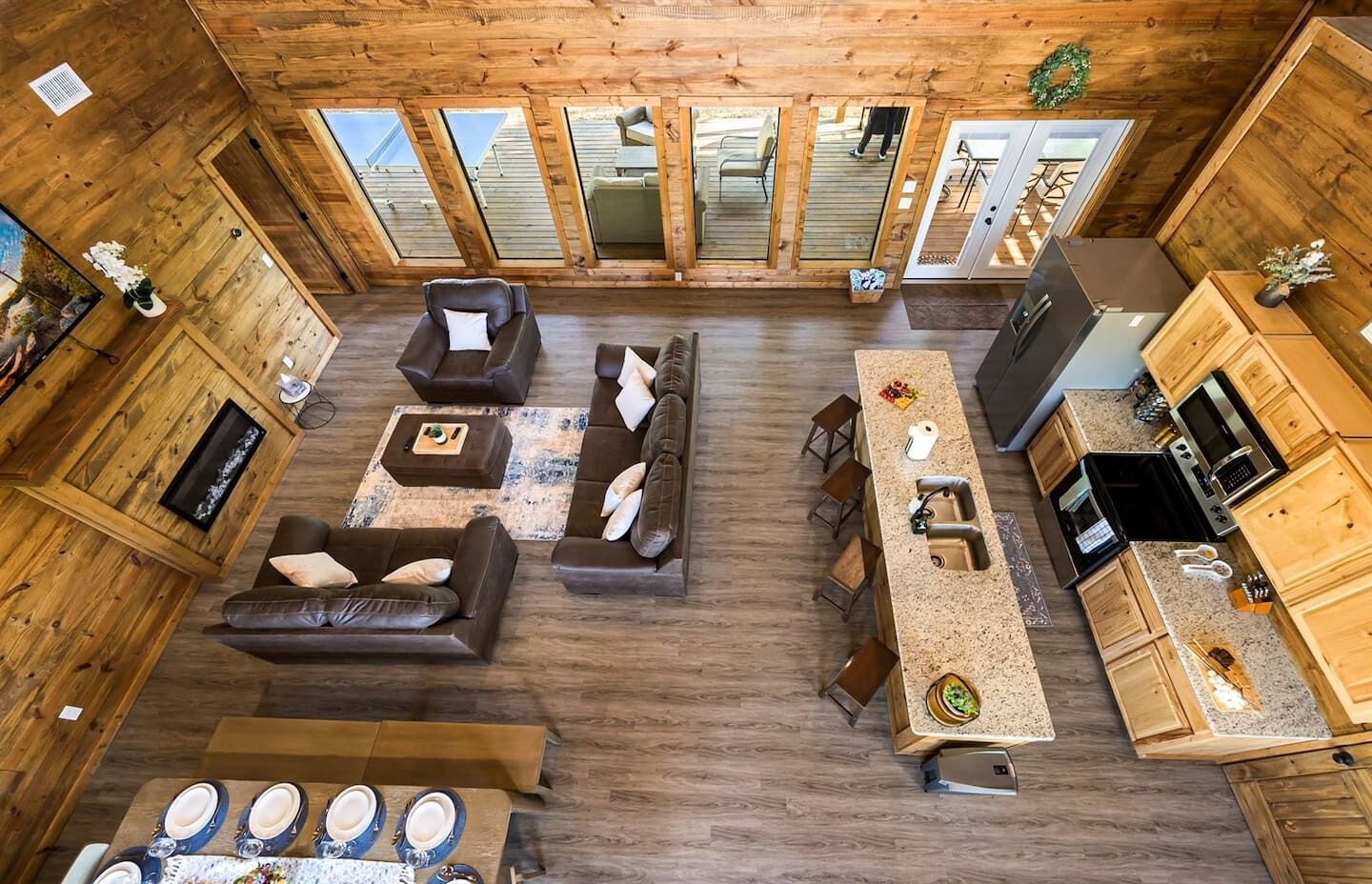 Amplio espacio tipo loft con interior de madera, que incluye un conjunto de sofás, una mesa de comedor con sillas, una cocina con electrodomésticos modernos y ventanas grandes que permiten la entrada de luz natural.