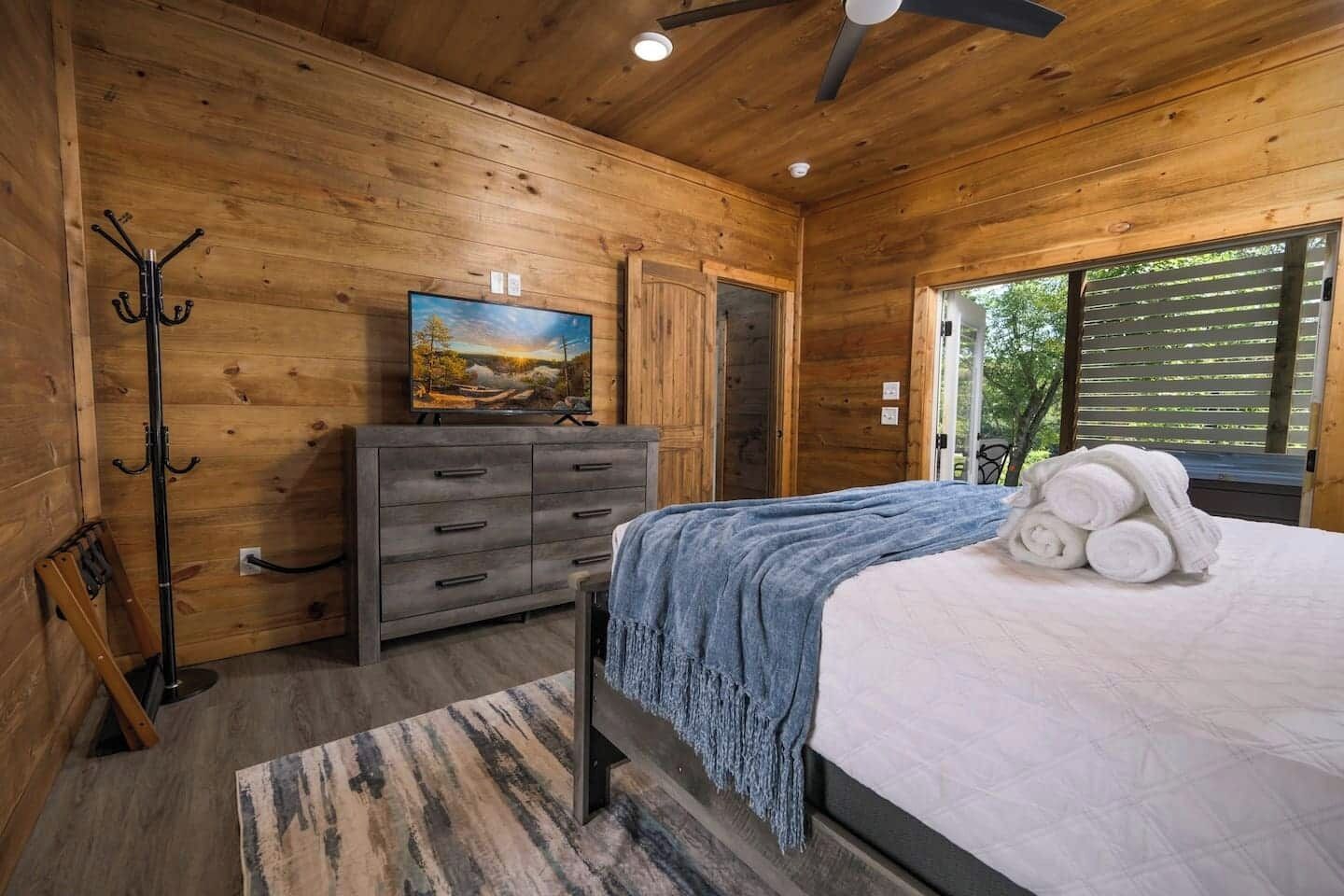Ein Schlafzimmer einer Holzhütte mit Bett, Kommode, Kleiderständer und einem Gemälde an der Wand.