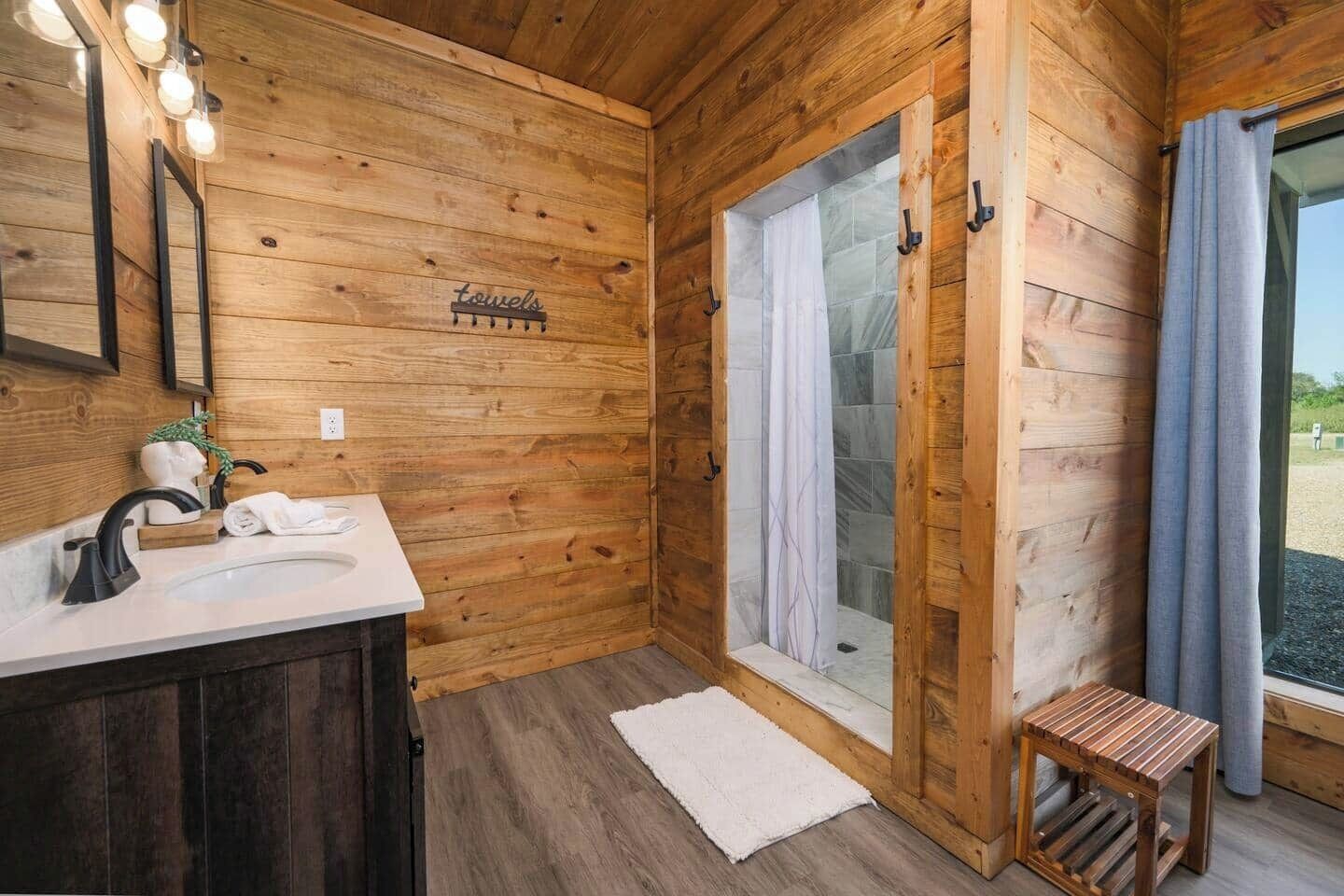 Un baño de cabaña de madera con lavabo, perchero y un taburete de madera pequeño.