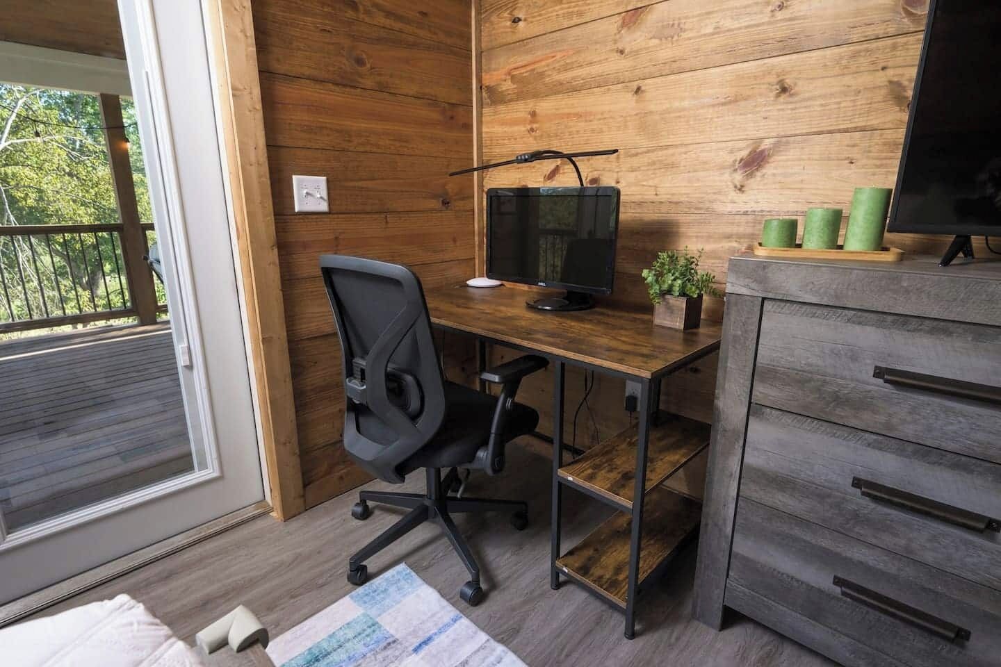 Een moderne kantoorruimte met een houten bureau, een zwarte bureaustoel, een computerscherm en een kleine plant.