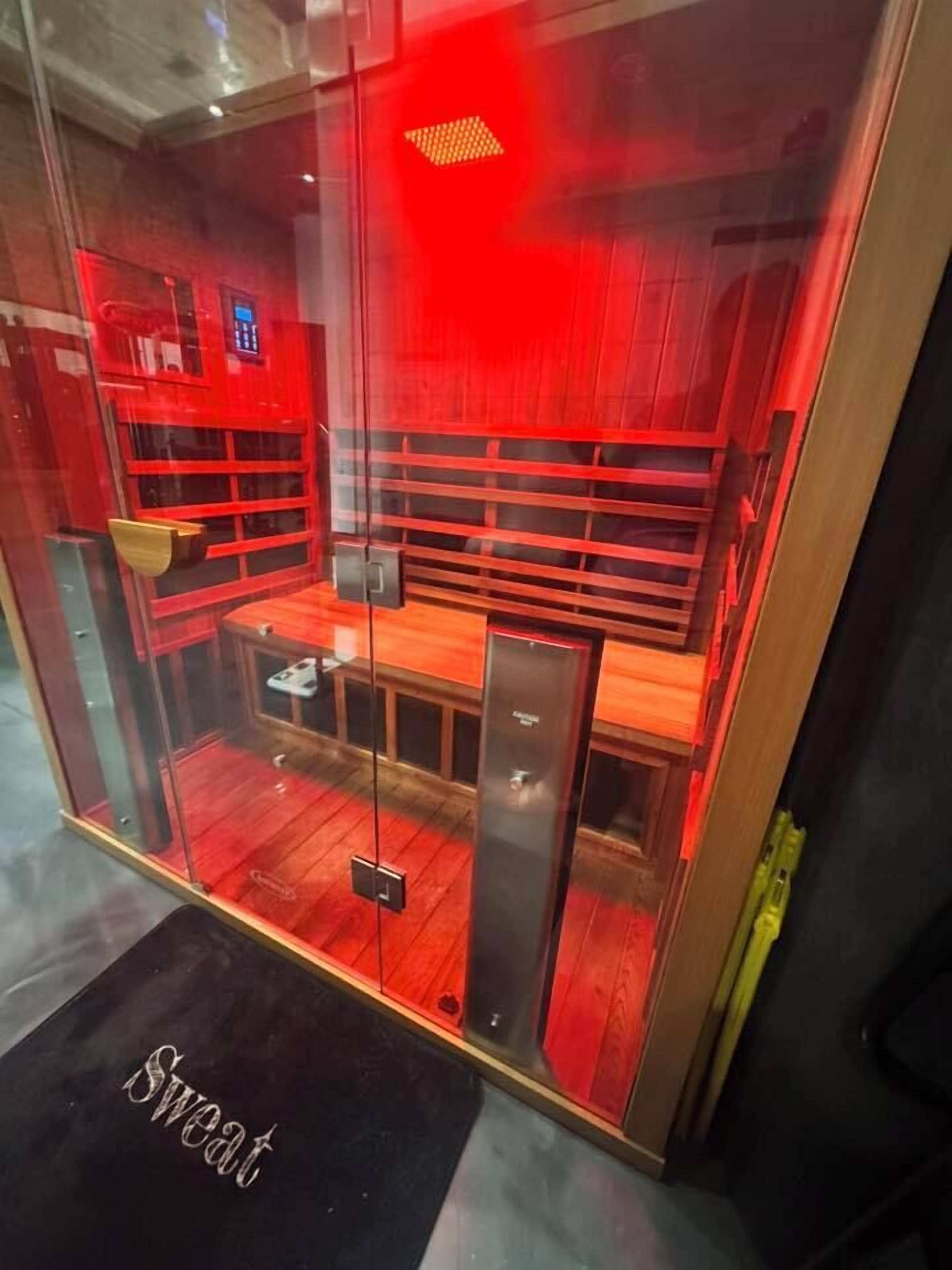 Ein raumhohes Fenster zeigt einen Innenraum mit roter Beleuchtung, eine Holzbank und einen kleinen Tisch.