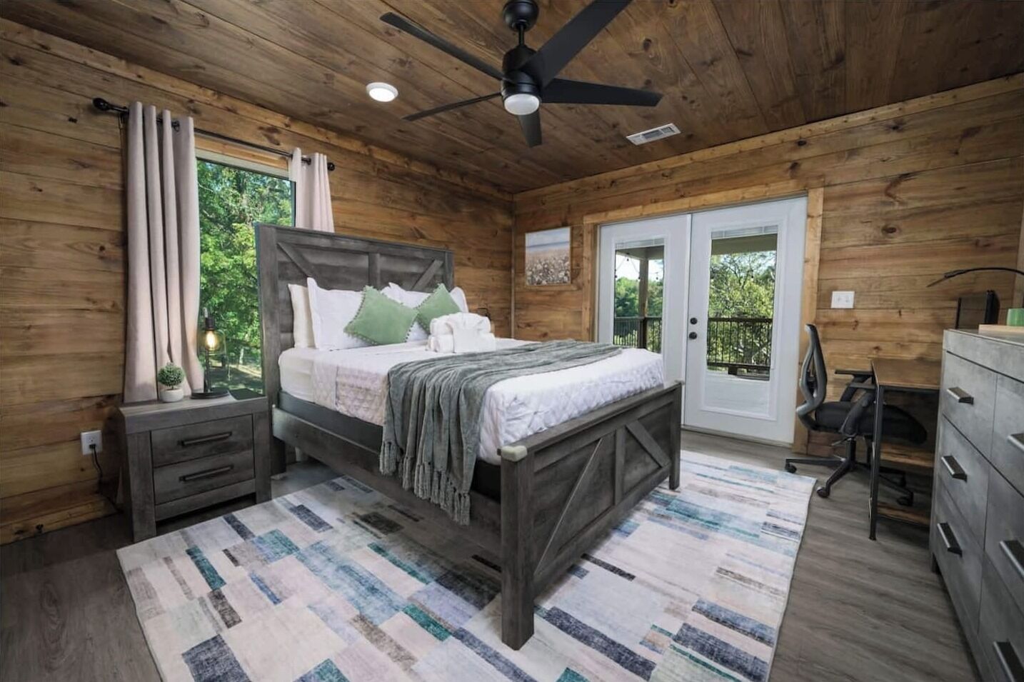 A wooden cabin bedroom with a bed, nightstands, a desk, and a ceiling fan.