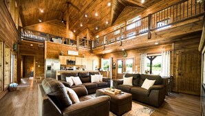 Un'ampia zona giorno con un grande divano in pelle marrone, un soffitto in legno e una cucina sullo sfondo.