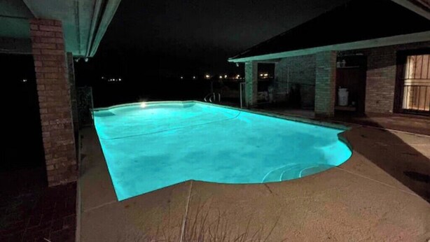 Una piscina de borde curvo, rodeada por un muro de ladrillo y un área de terraza cubierta.