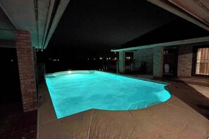 Una piscina de borde curvo, rodeada por un muro de ladrillo y un área de terraza cubierta.