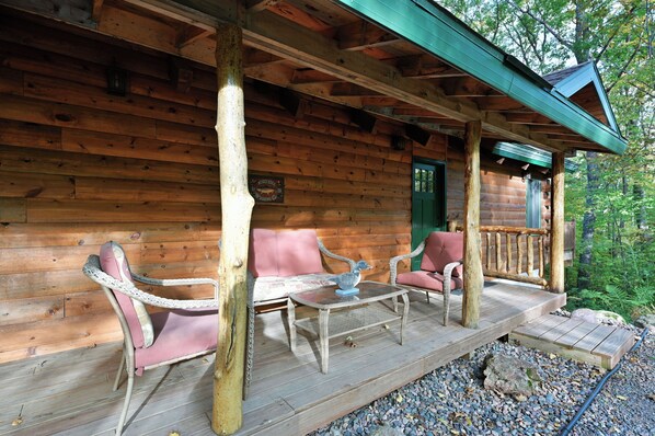 Eine Holzhütte mit Veranda, möbliert mit Korbstühlen und einem Tisch, und einer grünen Tür.