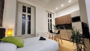A modern room with a bed, a desk, and a kitchenette.