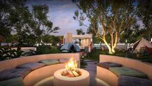 Un espace circulaire aménagé avec des sièges et un foyer, entouré d’une végétation luxuriante et d’arbres.