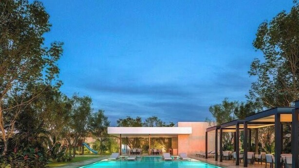 Une piscine dotée de chaises longues et d’un espace de repos couvert, le tout entouré d’arbres et d’un bâtiment.