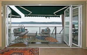 Relax on the balcony with a sofa, armchair, and coffee table, taking in the serene views of the calm body of water and distant hills.