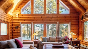 L’intérieur d’une cabane en rondins, avec un plafond mansardé, de grandes fenêtres et un coin salon confortable.