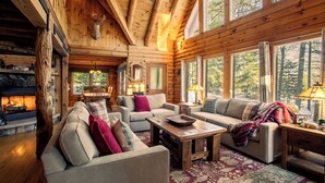 L’intérieur d’une cabane en rondins, avec une cheminée, des meubles en bois et de grandes fenêtres.
