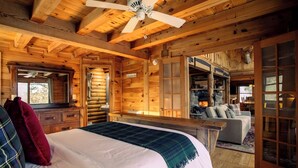 L’intérieur d’une cabane en rondins, avec un lit, un ventilateur de plafond, une cheminée et un canapé.