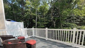 A wooden deck with white railings, wicker furniture, and a view of trees.