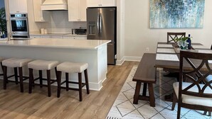A modern kitchen with white cabinetry, a stainless steel refrigerator, and a central island with bar stools.