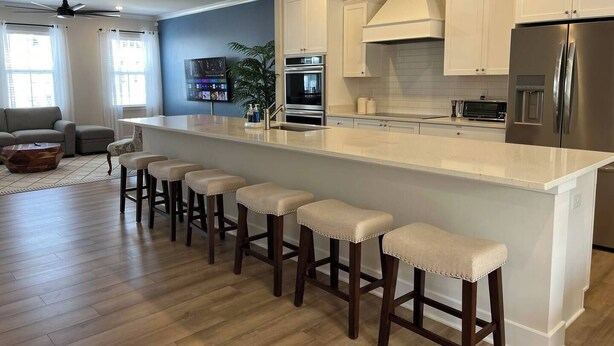 A modern kitchen with a central island, bar stools, stainless steel appliances, and a large window.