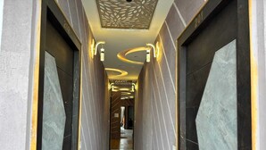 A modern hallway with dark marble walls, a glossy tiled floor, and contemporary lighting fixtures. - Hotel Guruvayur Dham (Mathura)