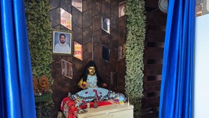 A room with a wooden partition, a small shrine with a framed photo, and a statue on a table. - Hotel Guruvayur Dham (Mathura)