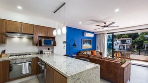 A modern kitchen with granite countertops, wooden cabinets, and stainless steel appliances. There is a dining area with a brown leather sofa and a table.