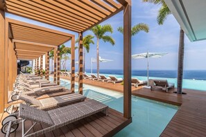 A poolside area with lounge chairs and umbrellas, overlooking a clear blue ocean. - SOHO PV Luxury Condo • Romantic Zone • Rooftop Infinity Pool • Ocean & City View (Puerto Vallarta)